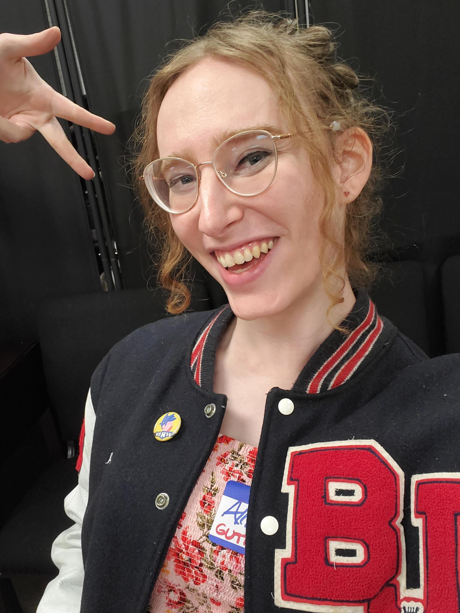 Allison Montgomery, a white woman, is looking at the camera and smiling casually. She is wearing a Bob Jones High School letterman jacket over a floral dress. She looks very electable, but it's dawning on her that she needs help to knock all the doors in District 25.