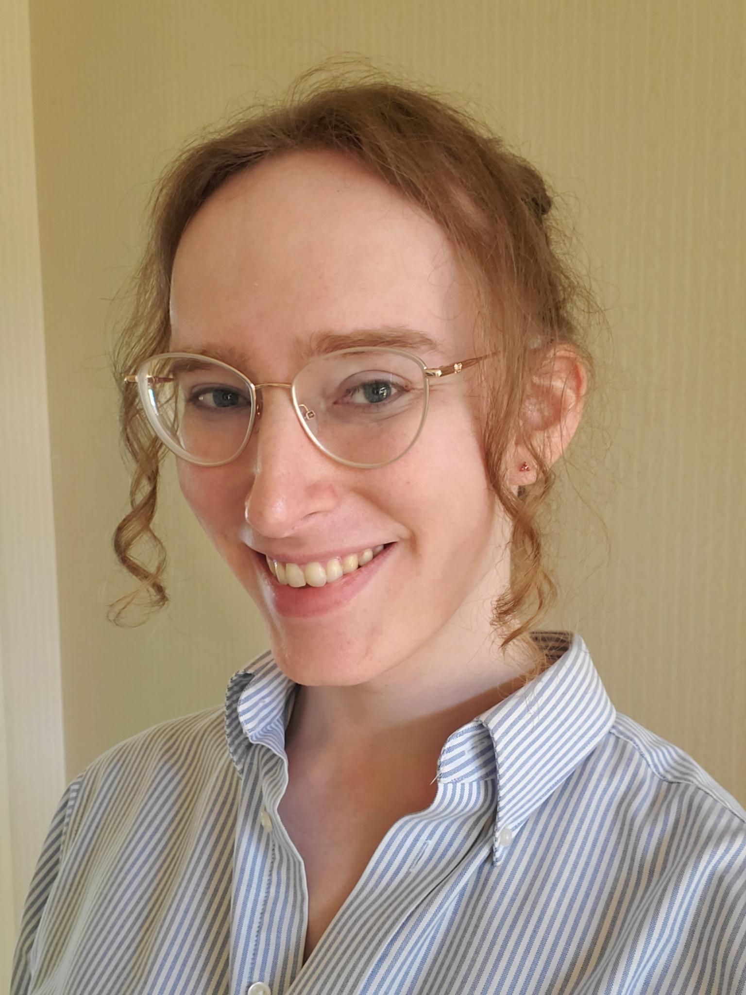 A photo of Allison Montgomery, a white woman, looking at the camera and smiling. She has long, sandy brown hair, which she is wearing up, except for two curly bangs, and is wearing a button-down shirt. She looks extremely electable.